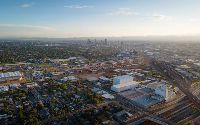 Aerial view over Denver neighborhoods toward the downtown skyline and the mountains at dusk.