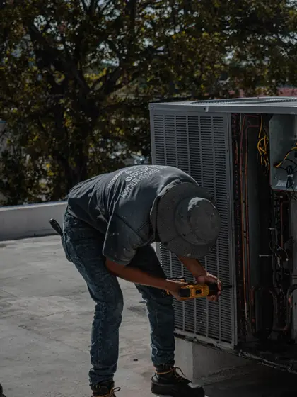 A technician in a cap testing an open outdoor cooling unit on a sunny roof.